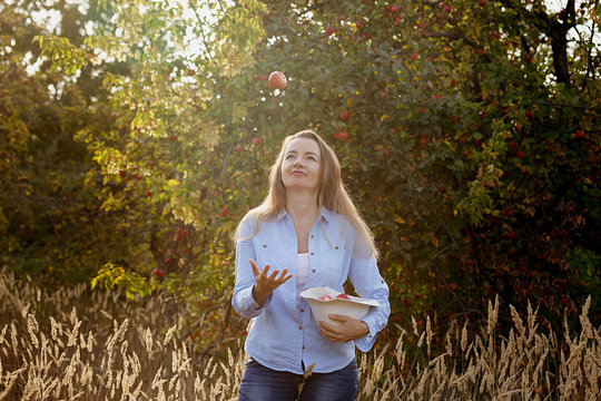 45 Year Old Happy Woman Throws Up An Apple In The Autumn Garden At Sunset