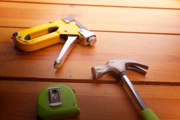 A hammer, measuring tape, and a staple gun are laying on a wooden surface