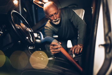 Interior car detailing. Senior beard man cleaning his car with vacuum cleaner in the evening at car...