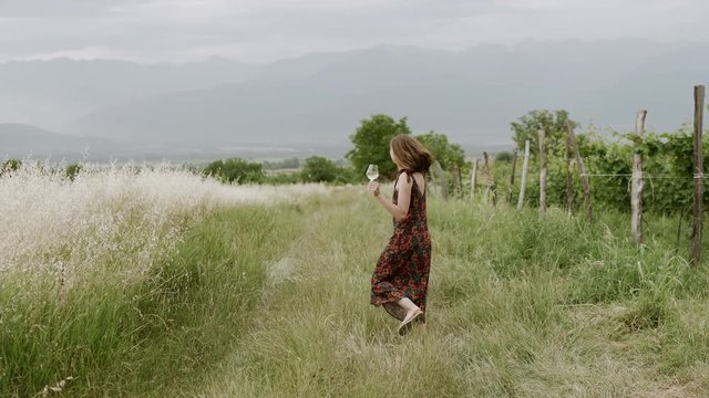 Happy woman dancing in vineyard with glass of wine. slow motion. handheld