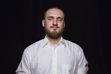 Obraz premium Close up portrait of young man isolated on black studio background. Photoshot of real emotions of male model with closed eyes. Thinking and smiling. Facial expression, human emotions concept.