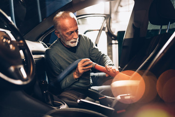 Interior car detailing. Senior beard man cleaning his car with vacuum cleaner in the evening at car...