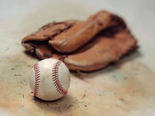 Worn and scuffed baseball and mitt on vintage canvas background with grass and dirt from the diamond
