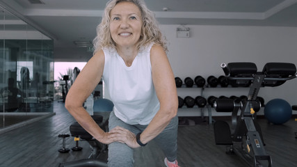 Fototapeta na wymiar Elderly woman makes squattings in the gym. Elderly woman Senior woman makes a sport exercises in the gym