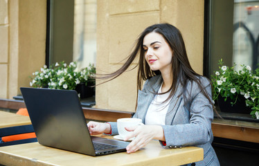 Young sucsessful business woman started working with laptop after coffee break at the street cafeteria