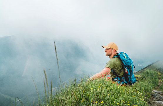 Tired backpacker man has a rest break enjoying cloudy valley bottom walking by the foggy cloudy weather mountain range . Active sports backpacking healthy lifestyle concept.