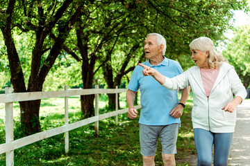 retired woman with grey hair pointing with finger near surprised husband