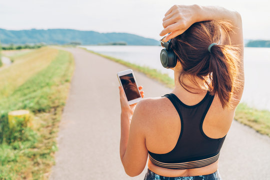 Young female starting jogging and listening to music using smartphone and  wireless headphones.