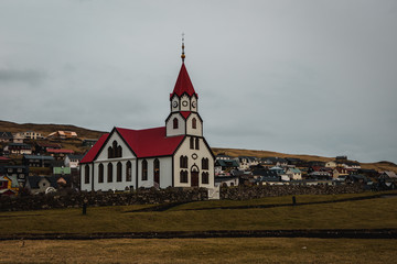 Sandavagur Church / Sandavags Kirkja during moody spring evening with glowing red roof situated in the picturesque village Sandavagur (Faroe Islands, Denmark, Europe)