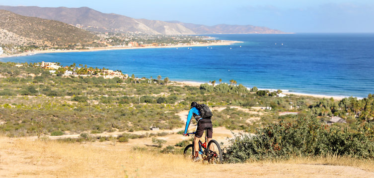 Man rides his mountain bike along a dirt trail in the Baja with the ocean in the background