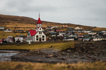 Sandavagur Church / Sandavags Kirkja during moody spring evening with glowing red roof situated in the picturesque village Sandavagur (Faroe Islands, Denmark, Europe)