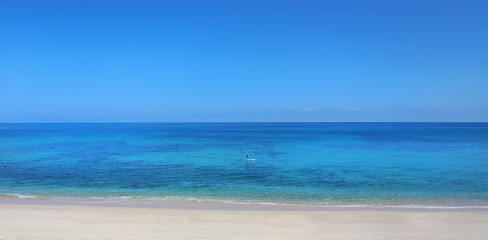 Fototapeta na wymiar Man on paddle board SUP on a calm blue ocean with clear blue skies. 