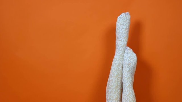 Legs of beautiful young woman in white fishnet tights on bright orange background