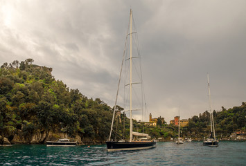 Obraz premium Malowniczy widok z morza na zatokę Portofino, słynną wioskę rybacką na Riwierze Liguryjskiej, z luksusowymi żaglówkami i jachtami zakotwiczonymi w małym porcie w pochmurny dzień, Genua, Liguria, Włochy