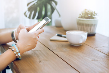 Closeup of girl hands using smartphone with cup of coffee and notebook on wooden table. selective focus soft and blurred background