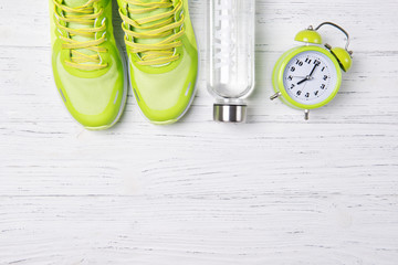 Fitness concept, green sneakers, alarm clock and bottle of fresh water on wooden background, top view, healthy lifestyle, morning training