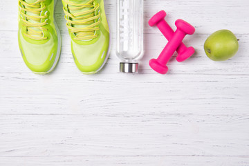 Fitness concept, green sneakers, pink dumbbells, bottle of water and green apple on a wooden...