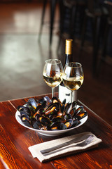 Fine dining in a seafood restaurant: a big dish of mussels with bottle of white wine with two wine glasses, on dark background