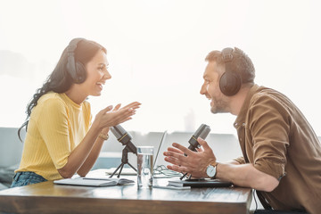 two cheerful radio hosts talking and gesturing while recording podcast in studio