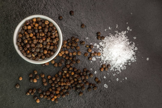 Sea Salt And Pepper Grains On Dark Stone Surface, Close Up..