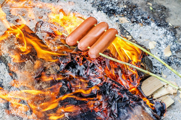 Grilling sausages over an open fire outdoors.