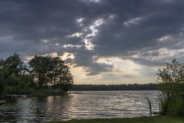 dramatische Wolken über See beim Sonnenuntergang mit Steg und Booten