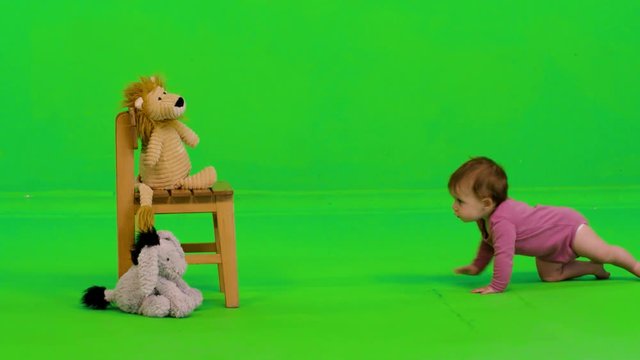 A lovely baby girl crawls to her puppets, stands, plays and drop her puppet over a green screen.