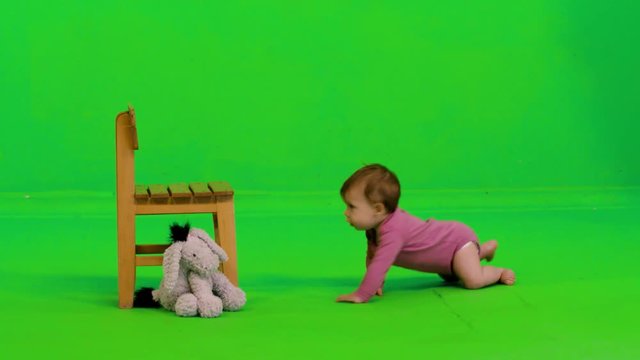 A baby girl crawls, stands using a chair, laughs happily and dance a bit, over a green screen.