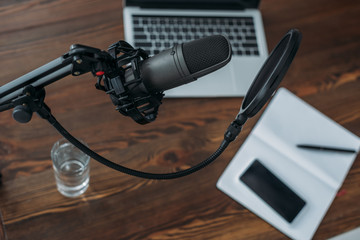 selective focus of microphone above wooden table with laptop, glass of water, notebook and smartphone with blank screen