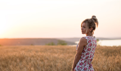 Fototapeta na wymiar young seductive rural blond hair woman in dress on the yellow wheat field on the sunset, lake on the background