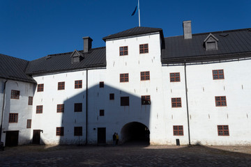 The courtyard, the white stone walls and the tower of the historic medieval castle Abo fortress in the city of Turku in Finland on a sunny summer day.
