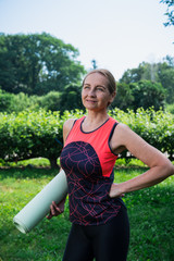 50 years old woman standing in a park with yoga mat