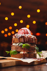 Huge layered cake with sponge biscuit, vanilla buttercream, banana, mint, topped with a big scoop of strawberry icecream and caramel topping on bokeh background