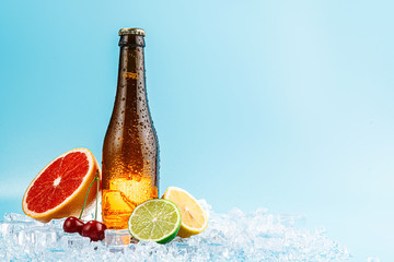 closed bottle of brown glass beer on ice. fruits lie nearby. concept of fruit craft beer or cider
