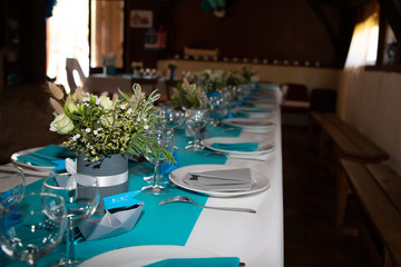 beautifully decorated white blue festive table with plates and glasses and bouquet of flowers in restaurant