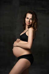 Beautiful young pregnant happy mother woman posing in underwear on dark 