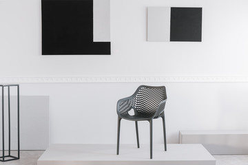 Fashionable grey metal chair on white platform in fancy showroom