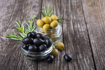 black and green olives in bowls, rosemary sprigs on wooden background. Organic food, healthy nutrition