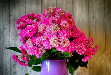 Beautiful bouquet of pink roses in a vase on the background of Provence planks