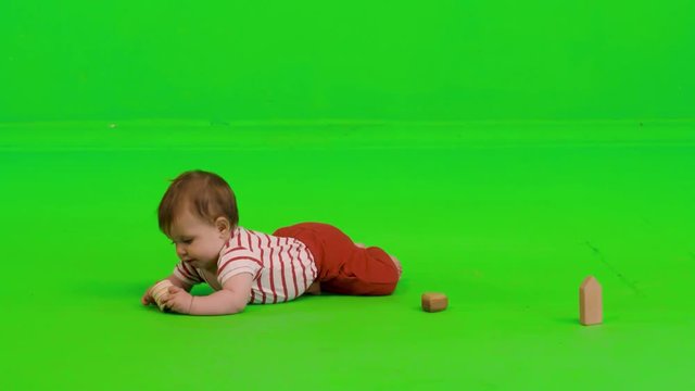 Playful baby plays happily with wooden toys over a green screen.