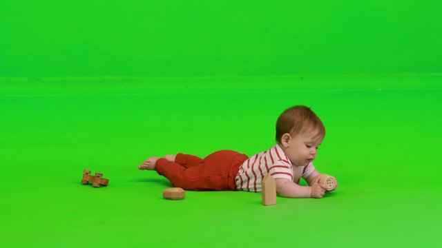 Cute baby girl plays happily with wooden toys over a green screen.