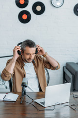 handsome radio host holding putting on headphones while looking at laptop