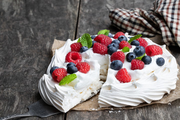 Pavlova meringue nest with berries and mint leaves on wooden table