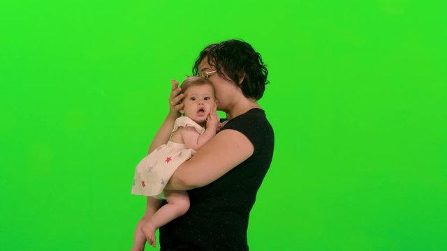 Young mom holds and hug her sleepy baby girl over a green screen.