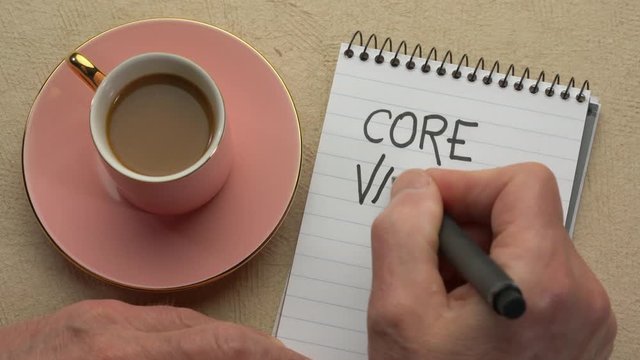 Core values - man hand writing a note with a black marker in a spiral notebook, overhead view