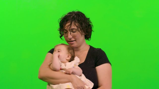 Beautiful mother holds and hug her sleepy baby girl over a green screen.