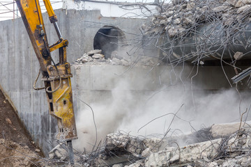 Professional demolition of reinforced concrete structures using industrial hydraulic hammer. Rods of metal fittings. Wreckage and crumbles of concrete.