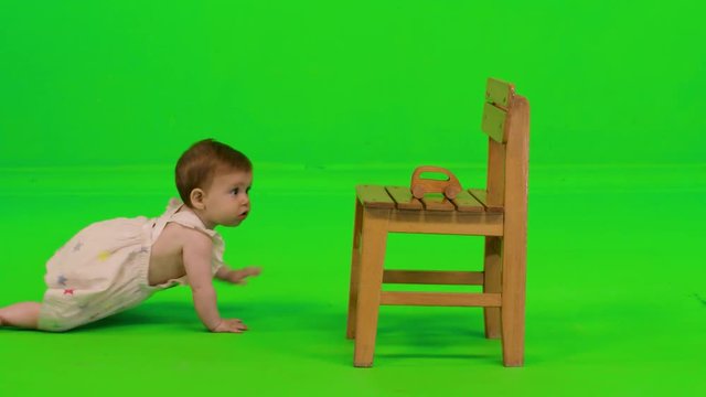 A lovely baby girl crawls to her toy, stands, plays and drops it over a green screen, wearing a dress.