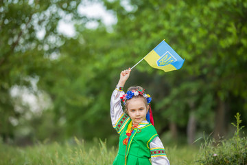 Little girl, wreath, embroidery, Ukrainian national costume with the flag of Ukraine. On the background of a green field
