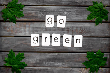 Go green text with green maple leaves on wooden background top view